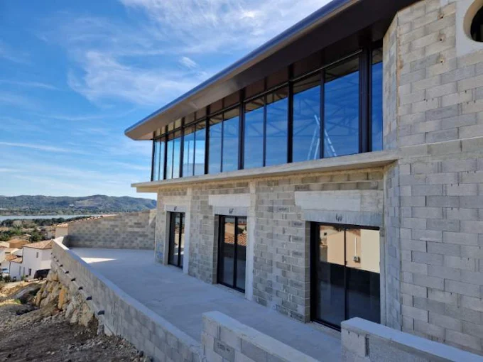 Maison moderne en pierre avec baies vitrées panoramiques surplombant lac