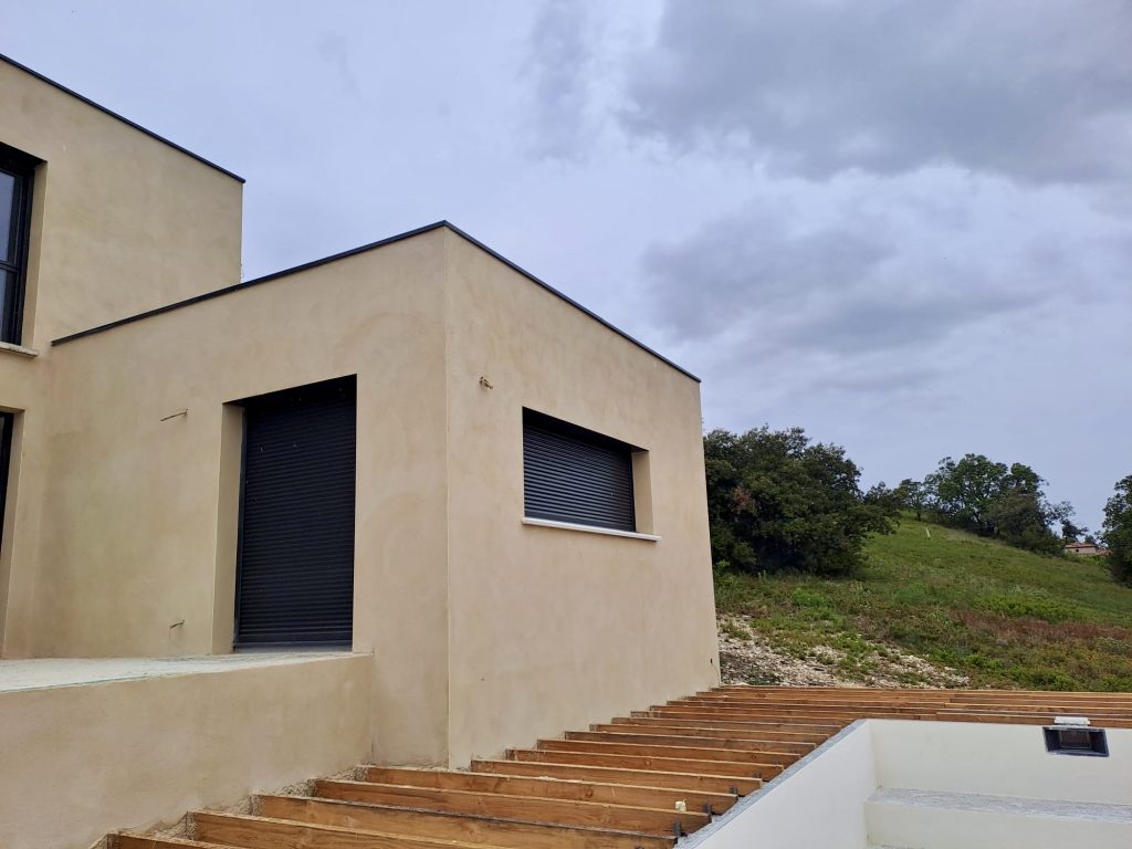 Maison moderne beige avec escalier bois et volets roulants noirs
