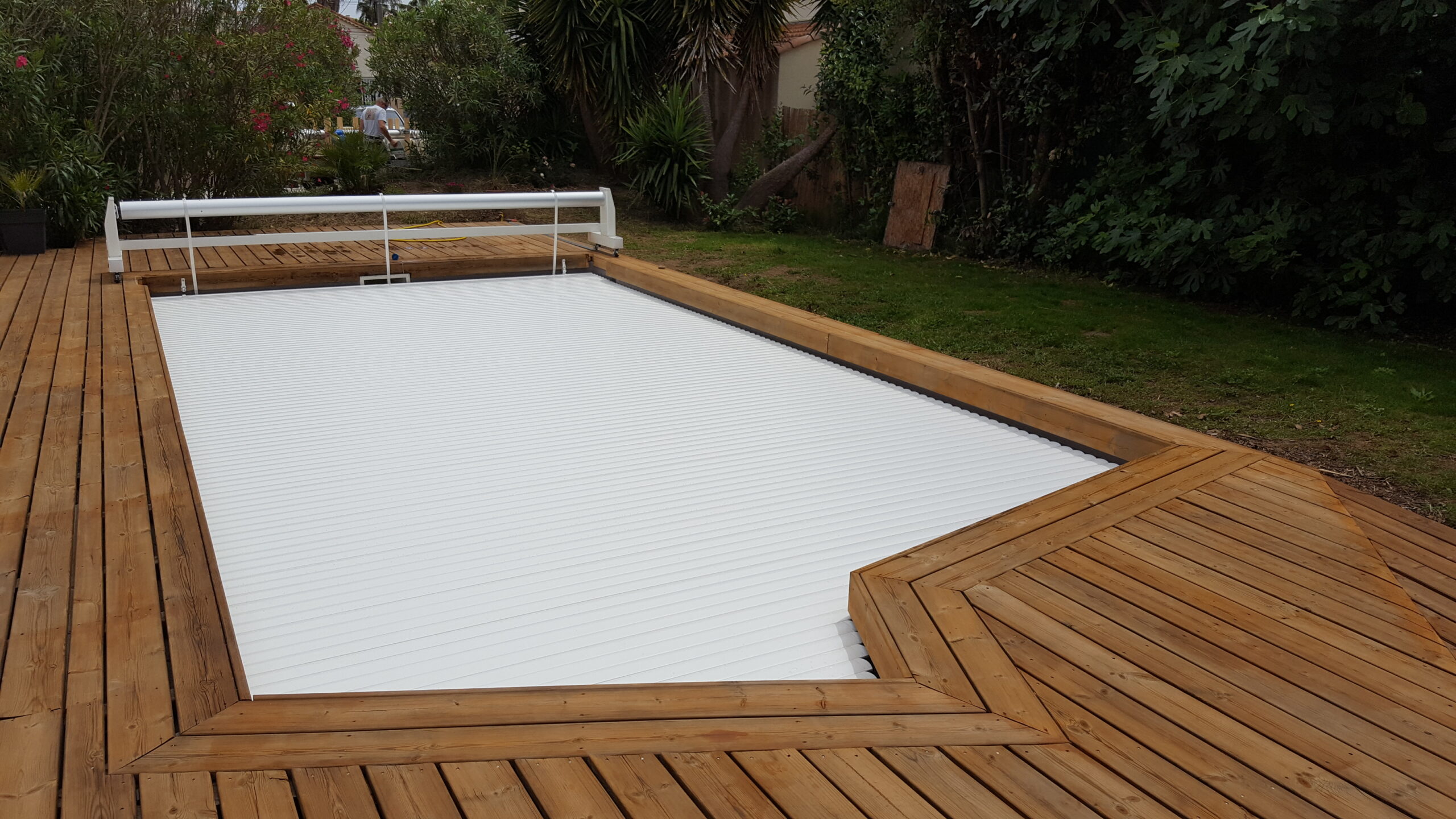 Piscine avec volet roulant blanc et terrasse en bois teck