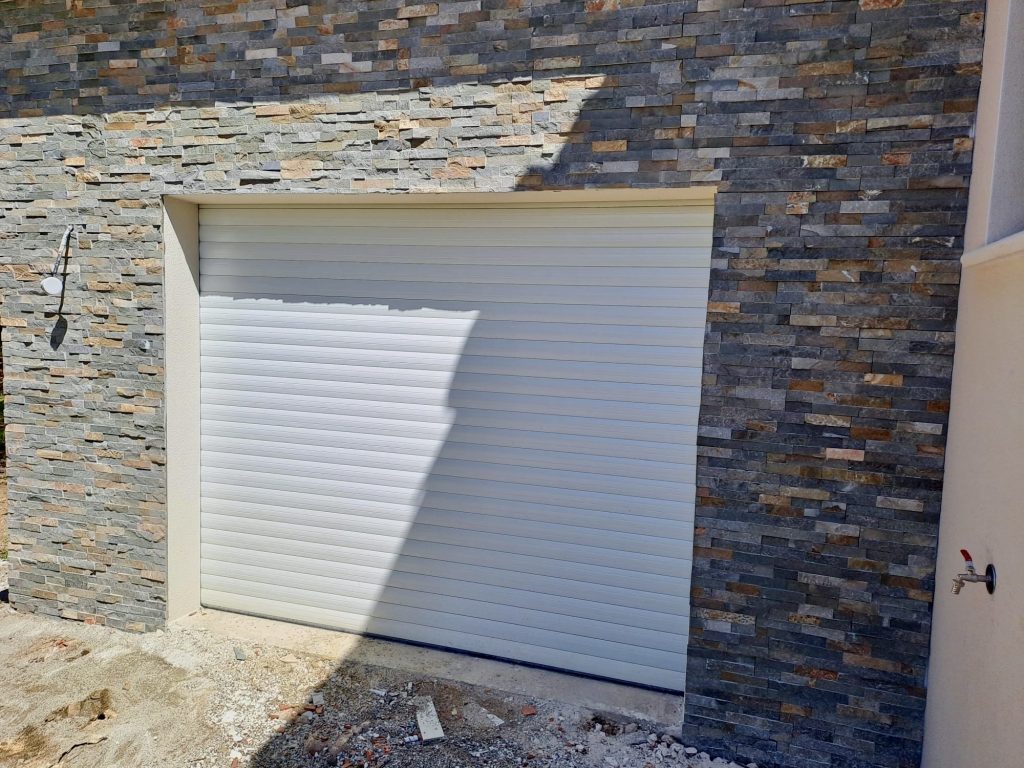 Porte de garage sectionnelle blanche intégrée dans façade pierre naturelle
